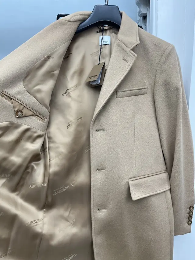 A stone-coloured wool overcoat hanging against a blue wall